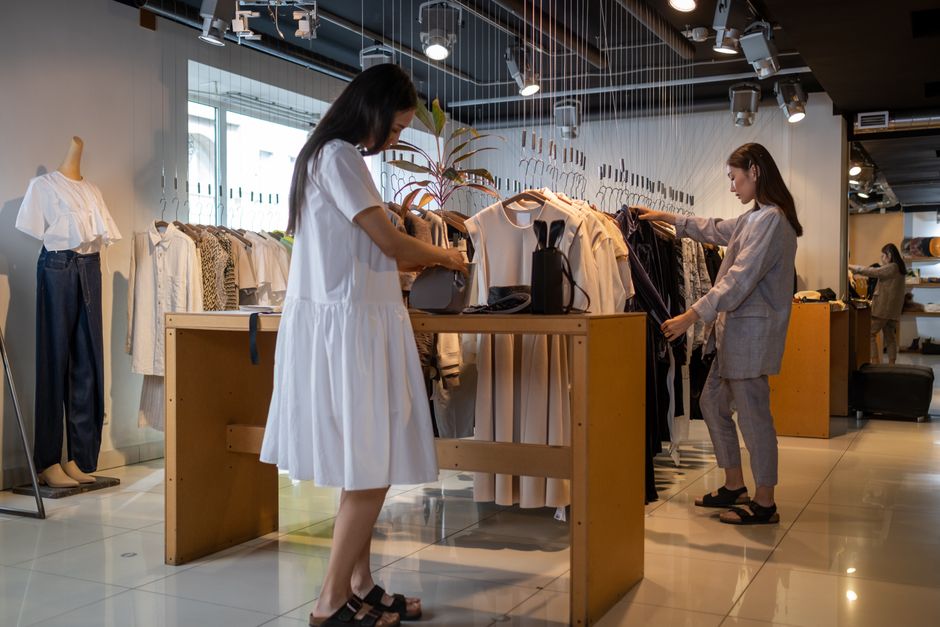 Two women browsing clothes in a modern indoor fashion store.